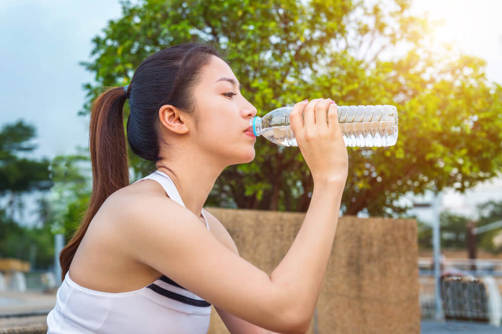 "sporty young woman drinking water after jogging"